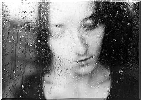 A sad woman looking out through a rainy window